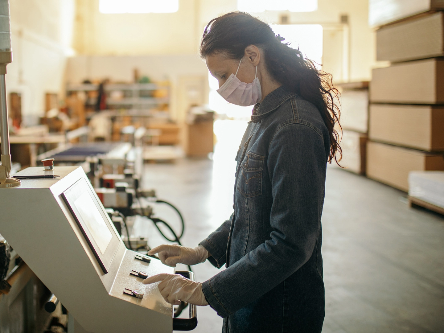 Frau arbeitet mit Mundschutz in einem Industriebetrieb an einer Maschine